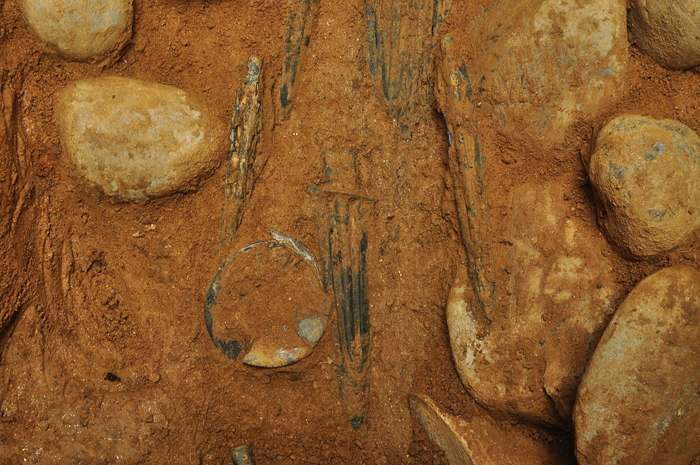 (Top) A diagram shows the layout of the bronze artifacts as they were found in the tomb. (Middle and bottom) The artifacts are covered with flat river stones. 
