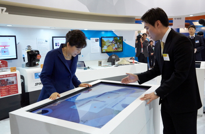 President Park Geun-hye tries out a set of smart devices at the Creative Korea 2014 fair, including a “3-D Virtual Fitting Room” (top) in which she tries on a variety of virtual dresses. 