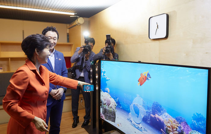 President Park Geun-hye (left) tries the smart TV application "3D Ocean," using both a smartphone and the smart TV to raise fish in a virtual reality aquarium.