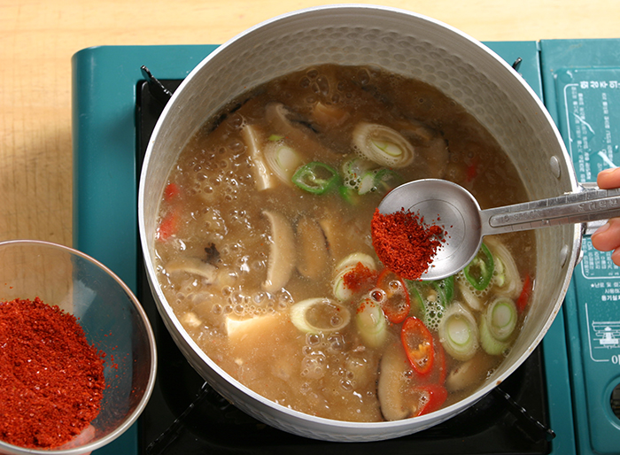 Add the tofu and red pepper powder to the pot. Boil it for 2 minutes. Add the red and green peppers and boil it for another 1 minute. Make sure to add the tofu and to boil it only a little bit so that it remains soft.
