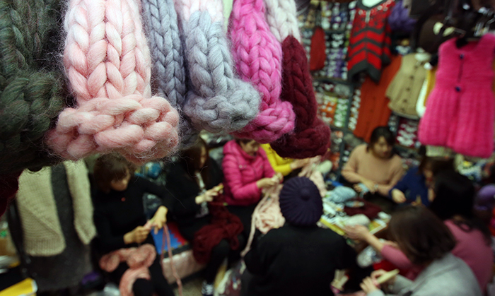 A group of young women huddle together, knitting their individual ski caps, at the Rose wool shop in the Dongdaemun Shopping Complex, Seoul.