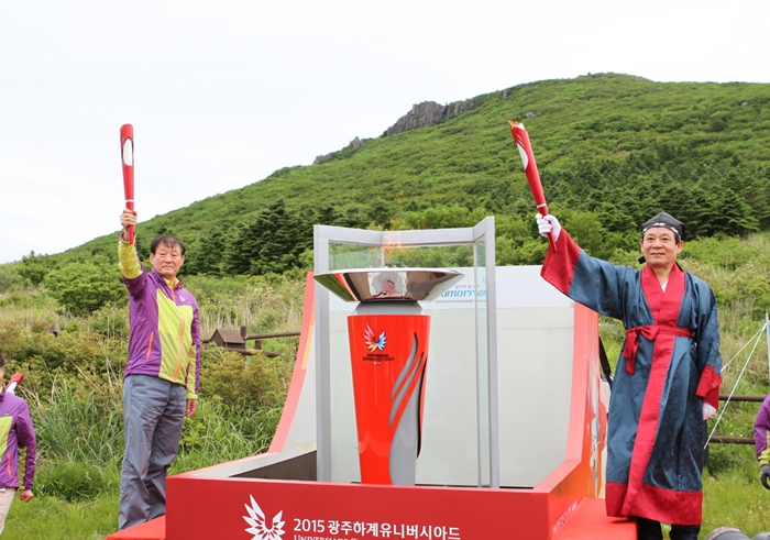 Gwangju Universiade Organizing Committee President Yoon Jang-hyun (right) and Vice President Kim Eung-sik hold up torches for the Gwangju Summer Universiade Games at the Jangbuljae mountain pass at Mudeungsan National Park after lighting the joint flame.