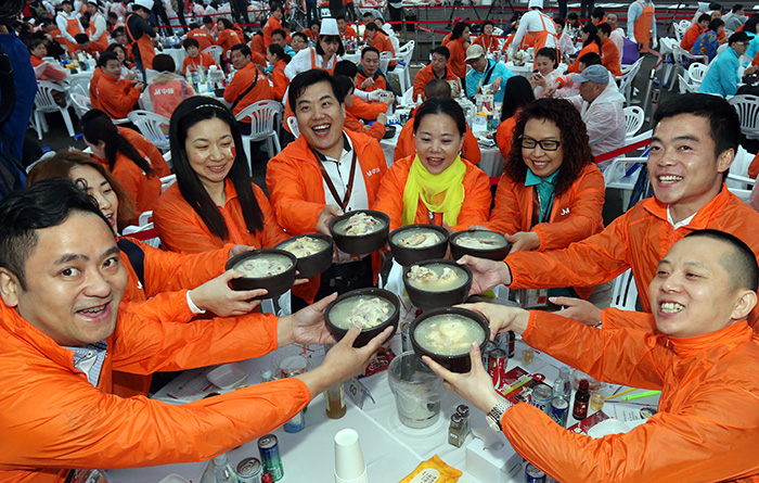 Employees of Nanjing Joymain Science & Technology smile as they hold up their bowls of <i>samgyetang</i> during a company-wide ginseng chicken soup dinner in Seoul on May 6.