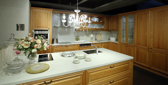 The above line of cabinets and countertops reflects the tastes of overseas customers who prefer a Western kitchen, including light wood-colored furniture, drawers with handles and a chandelier.