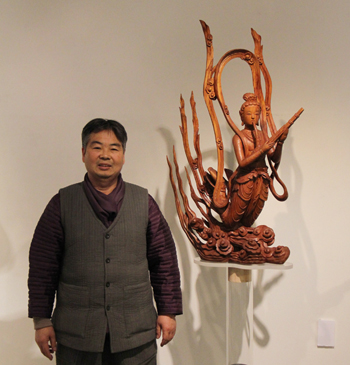 Artisan Heo Kil-yang stands next to his favorite, “A <i>Bicheon</i> Playing a Reed Aerophone,” just one amongst the 33 bicheon statues made of pine on exhibit at his ongoing “Pine Trees Become <i>Bicheon</i>” exhibition at the Seoul Arts Center. (Photo: Sohn JiAe)