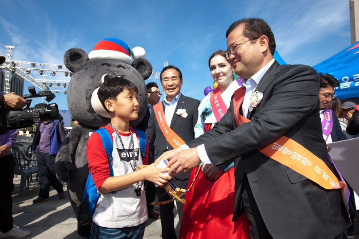 A promotional campaign for GenieTalk, a translating app, is held in Gwanghwamun Square in downtown Seoul on Oct. 9. Second Vice Minister of Science, ICT and Future Planning Choi Jae-yoo (right) offers a USB with GenieTalk on it to a young visitor.