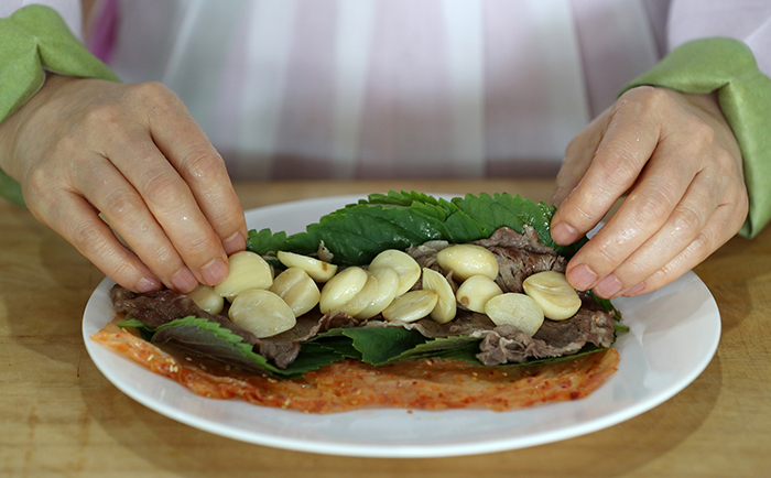 Unfold the well-fermented kimchi leaf and place some perilla leaves, the pan-fried beef and the garlic on top. Roll it all together.