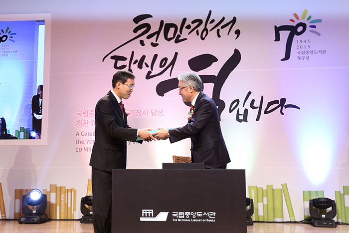 Minister of Culture, Sports and Tourism Kim Jongdeok (right) passes the 10 millionth book to National Library of Korea Chief Executive Lim Wonsun.