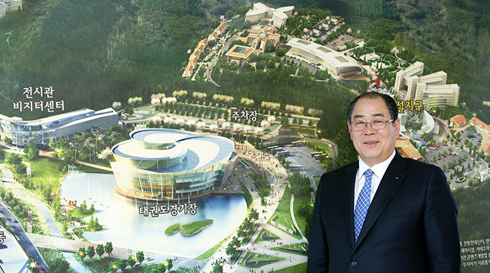 Muju-gun County Mayor Hwang Jeongsu stands beside an artist's rendition of the Taekwondowon. He recommends that all non-Korean tourists visit the martial art center. 