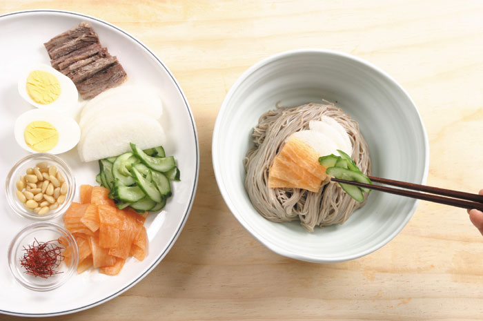 Put the noodles in a bowl and decorate it with beef slices, cucumber, radish, egg, pear, pine nuts and shredded red pepper. Pour the cold broth overtop before serving.