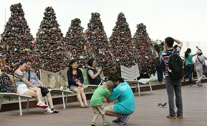 Chinese tourists pose for photos in front of the 'Trees of Love' padlock formations at N Seoul Tower atop Namsan Mountain in Seoul on July 22. There are seven tree-shaped frames covered with padlocks at the base of the tower. (photo: Jeon Han)