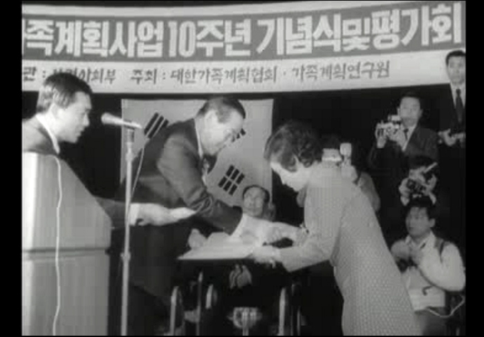 An award is given out during a ceremony to mark the 10th anniversary of a family planning program in 1971. The Family Planning Association of Korea actively carried out various birth control programs in those days. The above is a TV image from Daehan News.