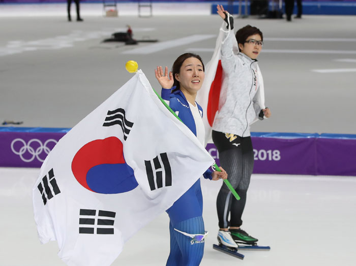 Lee Sang-Hwa (left) and Nao Kodaira wave to the crowd as they circle the rink after finishing the women's 500 m speed skating final, at the Gangneung Ice Arena on Feb. 18. (Yonhap News)