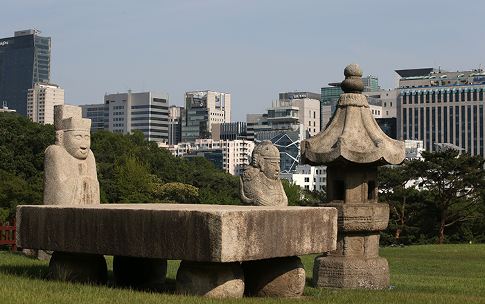  Stone statues of a civil servant and a military officer guard the Seolleung Tomb. High-rises unfold like a screen in the background. 
