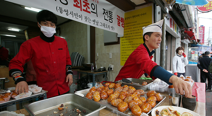 Young merchants on a street in front of the Tongyeong Jungang Market recommend some traditional honey bread to passersby. 