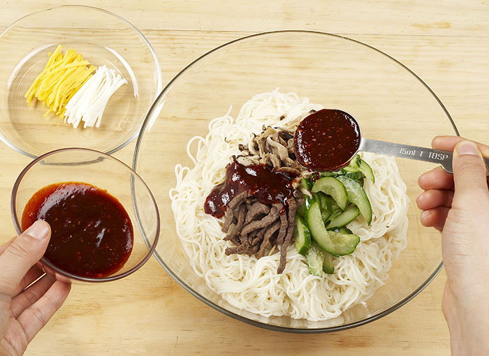 <i>Bibim guksu</i> is served with cooked noodles, beef, mushrooms, cucumber slices and fried egg yolks and fried egg whites, as well as with marinade No. 2. 
