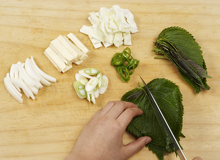 Trim and wash all the vegetables, including the sweet potato, onion, cabbage and sesame leaves. Cut them into thin, bite-sized pieces.