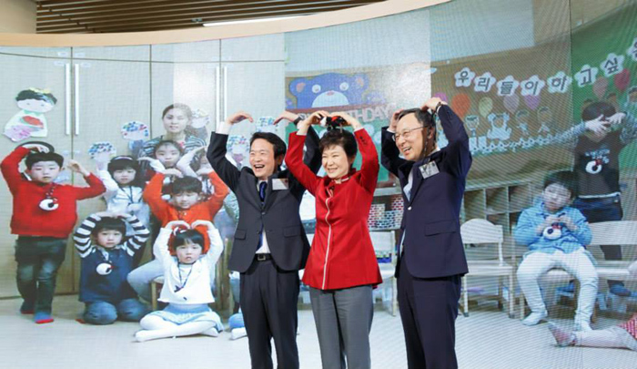 President Park Geun-hye (middle) makes a heart sign with her arms along with children at a daycare center after testing a live video feed that shows the inside of the daycare center. 