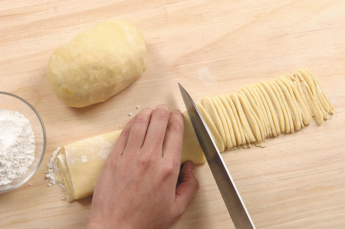 Wrap the dough with a cotton cloth and let it sit for 30 minutes. Press and roll it with a wooden rolling-pin until it's 0.2 cm thick. Sprinkle on some additional flour over the top. Roll the sheet again and cut it into slices 0.2 cm wide.