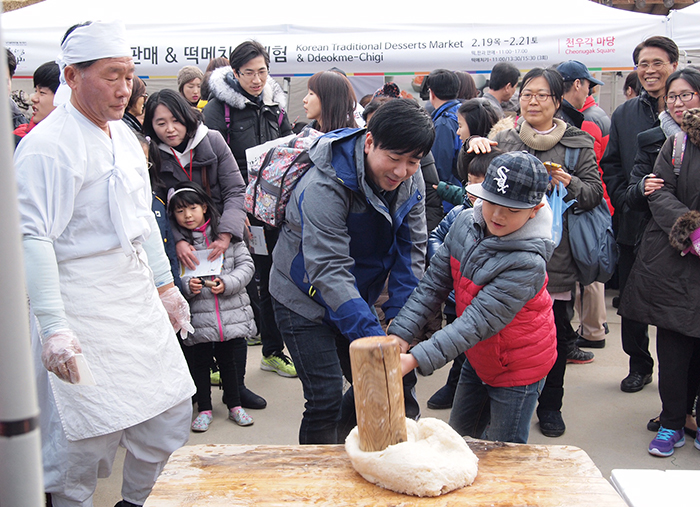 Festival-goers try their hand at pounding rice cake dough at the Namsangol Hanok Village in Seoul.