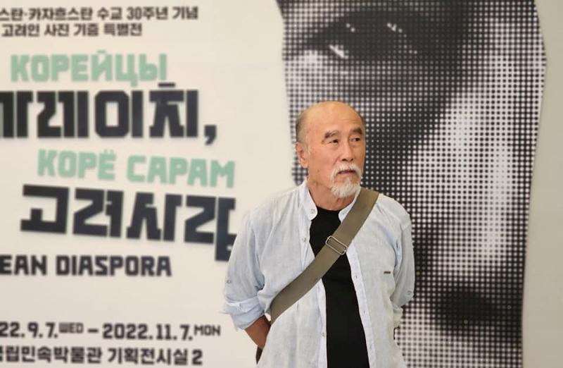 Korean Uzbek photographer Viktor An poses in front of the promotional poster for his exhibition 