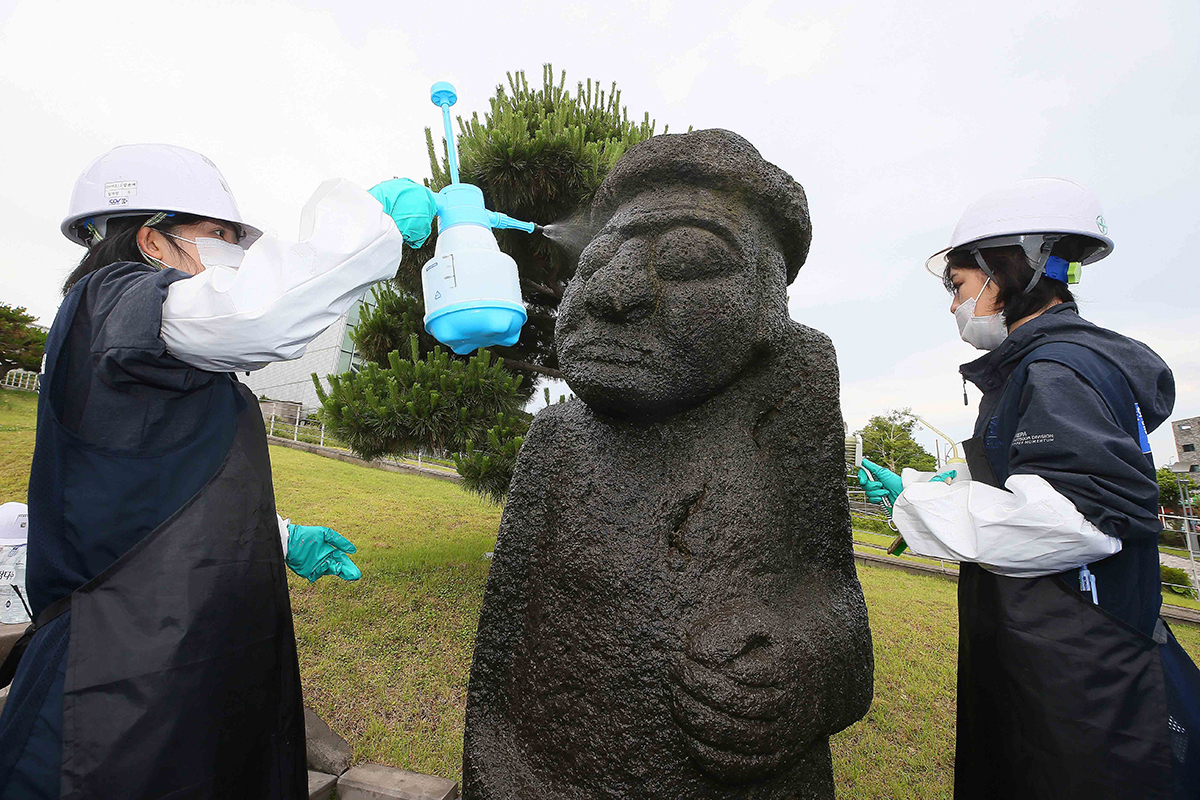 Staff from Jeju Center for the Care of History and Cultural Heritage (unofficial translation) under a foundation for promoting Jeju Island's culture on the morning of June 8 clean a dol hareubang, or a large folk rock statue whose name literally means (stone grandfather,) in front of the entrance of the KBS Jeju Broadcasting Branch Office.