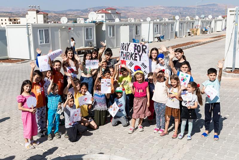 Turkish children on Oct. 7 hold drawings and letters thanking the Korean people and a large poster drawn by students at Kyonggi Elementary School in Seoul while posing for a group photo at the move-in ceremony for Korea-Turkiye Friendship Village in the town of Pazarcik in Kahramanmaras province in Turkiye (Turkey). 