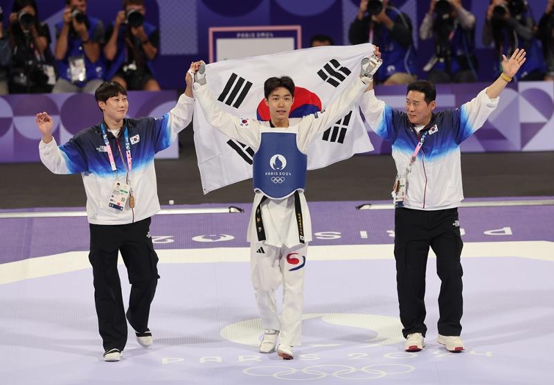 Park Taejoon (middle) on Aug. 7 celebrates while holding the Korean national flag Taegeukgi after winning the men's taekwondo 58-kg class at the Paris Summer Olympics held at the Grand Palais in Paris.