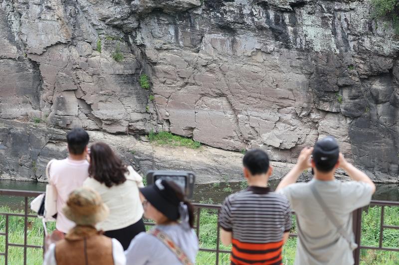 Visitors on July 13 take selfies of the Petroglyphs, or prehistoric images carved on rock, along Bangucheon Stream at Bangudae Petroglyphs Observatory in Daegok-ri Village of Ulsan's Ulju-gun County. Including those in the villages of Daegok-ri and Cheonjeon-ri, the petroglyphs were registered on July 12 as UNESCO World Heritage. (Yonhap News)