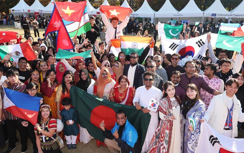 Foreign exchange students wearing the traditional clothes of their home countries on Nov. 7, 2024, wave their national flags and smile on Ajou International Day, an event at Ajou University in Suwon, Gyeonggi-do Province. (Yonhap News)