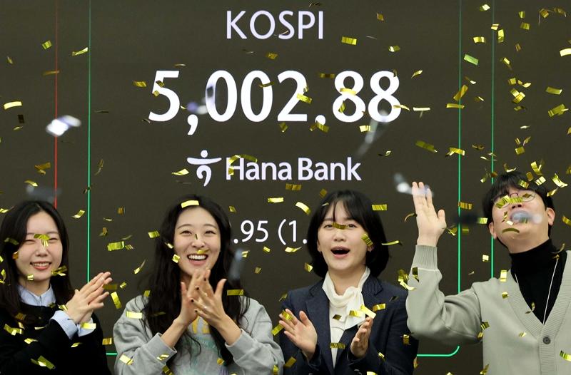 The main stock market index KOSPI on Jan. 22 crossed the 5,000 mark for the first time in history in early morning trade. Shown are dealers that day celebrating the milestone in front of the electronic billboard at the dealing room of Hana Bank headquarters in Seoul's Jung-gu District. (Yonhap News)  