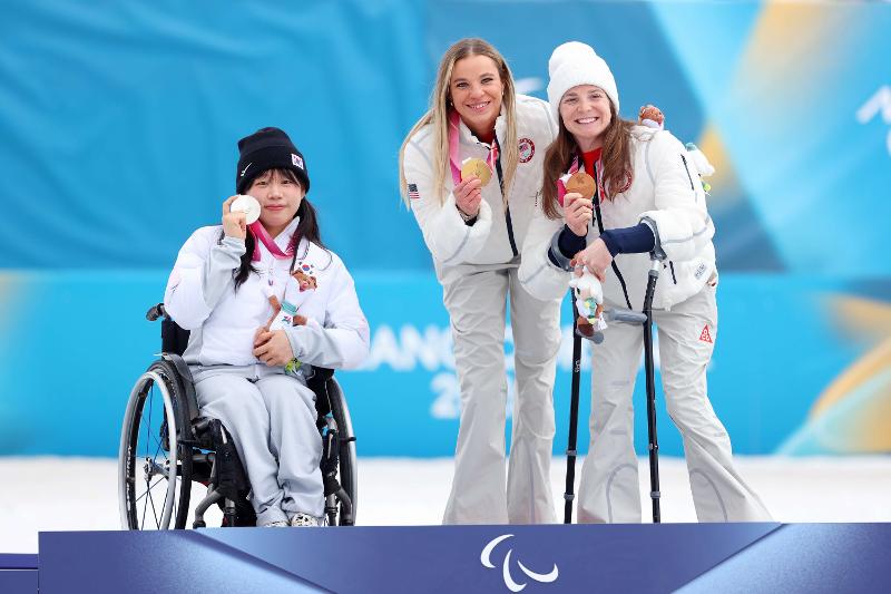 Kim Yunji (left) on March 11 poses with her silver medal in the 10-km interval start sitting race of cross-country skiing on the winners' podium of the Milan Cortina Winter Paralympics in Italy at Tesero Cross-Country Skiing Stadium in the village of Tesero. 