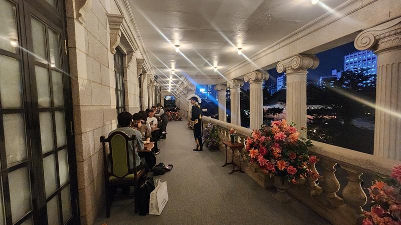 A staff member dressed in a Korean Empire military uniform on Sept. 16 greets visitors while they have drinks and snacks against the backdrop of the evening view from the second-floor terrace of Seokjojeon Hall at Deoksugung Palace in Seoul. (Lee Jihae)